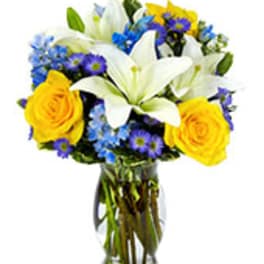 Bouquet of white lilies, yellow roses, and blue flowers in a glass vase
