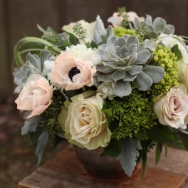 Soft pink and white flowers arranged with gray succulents in a bowl vase.