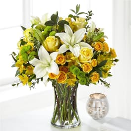 Tall bouquet of white lilies, yellow roses, and green mums in a clear glass vase