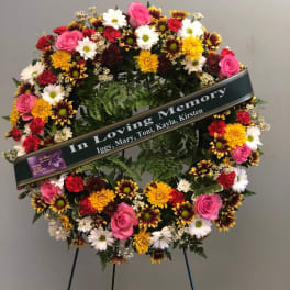 Circular sympathy wreath with pink roses, daisies, and mums on a stand