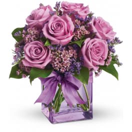 Pink roses arranged in a purple glass vase with a ribbon