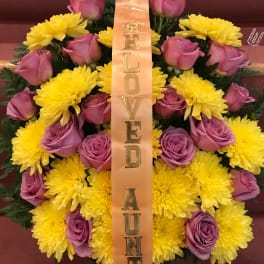 Pink roses and yellow chrysanthemums with a vertical ribbon reading "BELOVED AUNT"