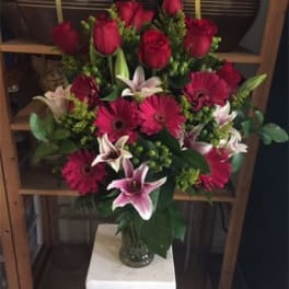 Bouquet of red roses, pink lilies, and magenta gerbera daisies in a glass vase