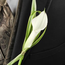 White calla lily boutonniere with striped greenery on a black suit lapel and patterned gold vest.