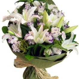Bouquet of white lilies and pale purple flowers wrapped in green paper