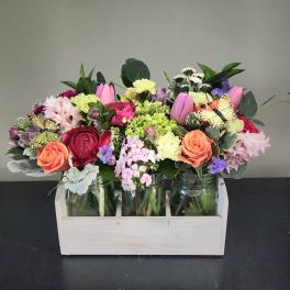 Colorful mixed flower arrangement in mason jars inside a light wooden crate