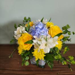 Yellow roses and white alstroemeria with blue hydrangea in a glass vase