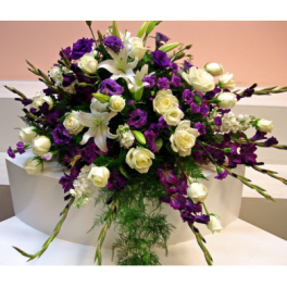 Purple and white floral arrangement with roses and lilies on a white pedestal