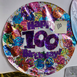 Round foil balloon reading Happy 100 Birthday with colorful confetti pattern