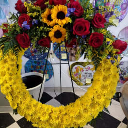 Heart-shaped floral wreath with red roses, yellow mums, and sunflowers on a stand