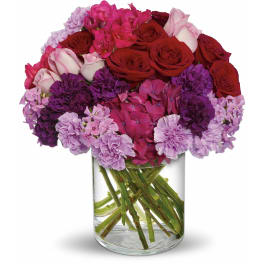 Bouquet of red and pink roses with purple flowers in a clear glass vase