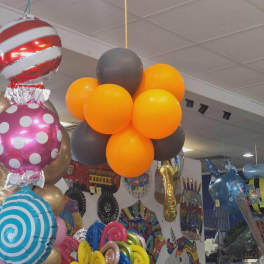 Clusters of colorful balloons hanging indoors, including orange, gray, and patterned foil balloons.