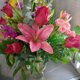 Mixed bouquet with pink lilies, red roses, and pink spray roses in a glass vase