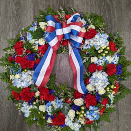Circular floral wreath with red, white, and blue flowers and a ribbon bow