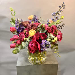 Mixed bouquet of pink, purple, and yellow flowers in a clear glass vase