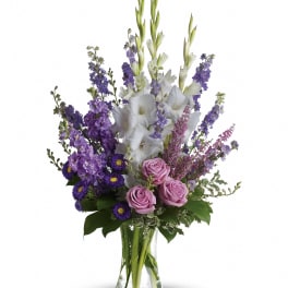 Tall purple and white flower arrangement with lavender roses in a clear glass vase