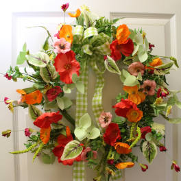 Colorful floral wreath with orange and red blooms on a white door