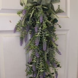 Hanging greenery swag with purple flowers and a large ribbon bow