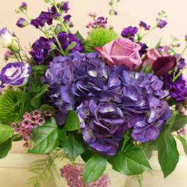 Purple hydrangeas and roses arranged in a decorative tin container
