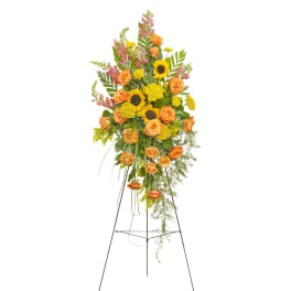 Tall standing spray of yellow sunflowers and orange roses with pink snapdragons on a metal easel