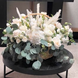 White rose arrangement in a wicker basket with eucalyptus and feathery accents