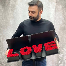 Man holding a black box arrangement spelling LOVE with red roses
