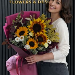 Woman holding a bouquet of sunflowers and small white flowers in pink wrap