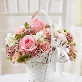 Pink roses and white flowers arranged in a white basket with a ribbon