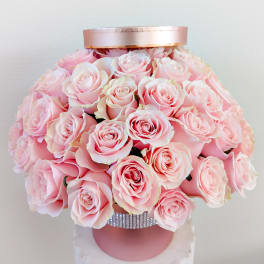 Pink roses arranged in a round hatbox with a satin lid and rhinestone band