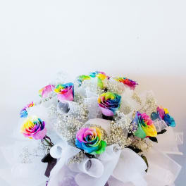 Rainbow roses in white wrap with baby's breath and a purple ribbon