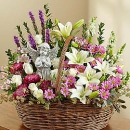 Basket arrangement of white lilies, pink flowers, and a small angel figurine