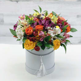 Mixed bouquet of orange, yellow, pink, and white flowers in a gray hat box