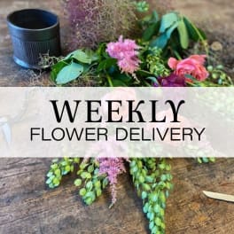 Loose floral arrangement with pink blooms and greenery beside a black container
