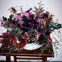 Purple floral arrangement in a white bowl vase