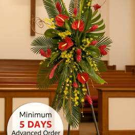 Tall tropical standing spray with red blooms and yellow accents on an easel in a church.