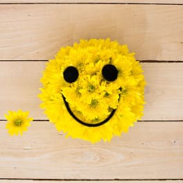 Round arrangement of yellow chrysanthemums shaped like a smiley face on a wood surface