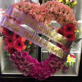 Heart-shaped floral wreath with pink roses and gerberas, with ribbon text