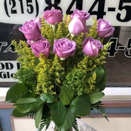 Pink roses arranged in a clear glass vase with yellow filler flowers