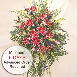 Tall standing spray with pink lilies and mixed white and yellow flowers on a metal easel
