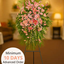 Tall pink standing spray of lilies and carnations with palm leaves on a black easel