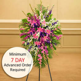 Tall standing spray with pink lilies and mixed purple and white flowers on a black easel stand