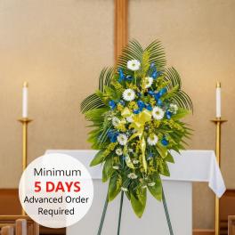 Standing funeral spray of white and blue flowers with yellow ribbon on an easel in a church sanctuary