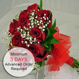 Hand-tied bouquet of red roses with small white filler flowers and a large red ribbon bow