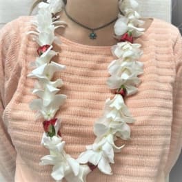 White flower lei with red accents worn over a peach sweater