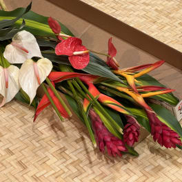 Bundle of assorted tropical flowers with large leaves laid in a cardboard box.