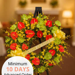 Standing sympathy wreath with red and green tropical blooms and yellow flowers on a black easel.