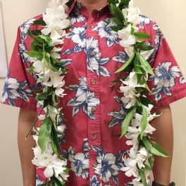 White floral leis with green accents draped around a neck over a red floral shirt