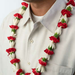 Red and white flower lei worn around a person’s neck over a light collared shirt
