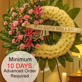 Standing sympathy wreath with white ring and pink lilies and carnations on a tripod stand