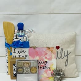 Gift set with pillow, kitchen utensils, positive message signs, and small boxed accessories.